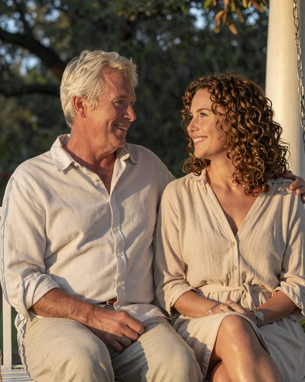 Mature American couple in their late fifties laughing together on a sunlit Charleston porch swing